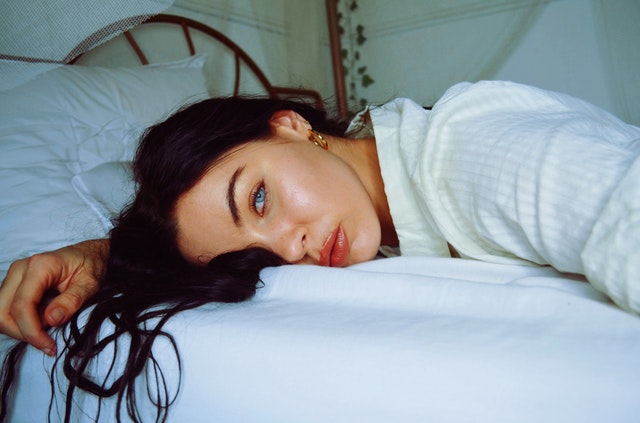 Sexy žena s modrými očami leží na bruchu v posteli.jpg